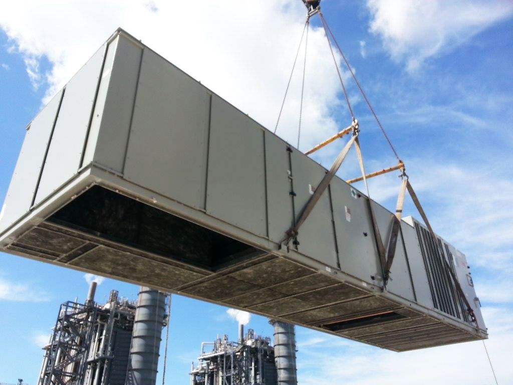 A large commercial air handling unit suspended from a crane during installation