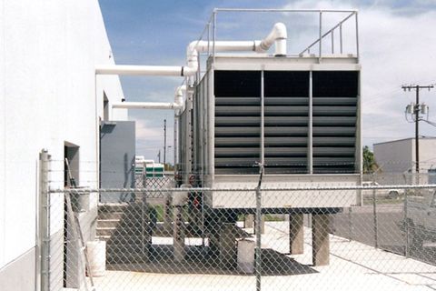 A cooling tower with white piping beside an industrial building