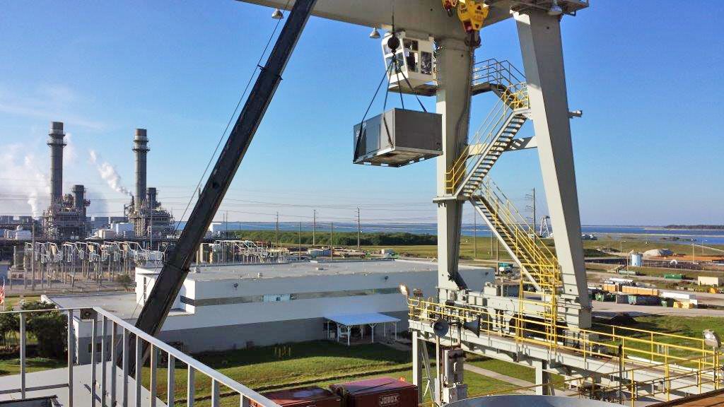 A gantry crane hoists a packaged air conditioning unit at a power plant on the Florida coast