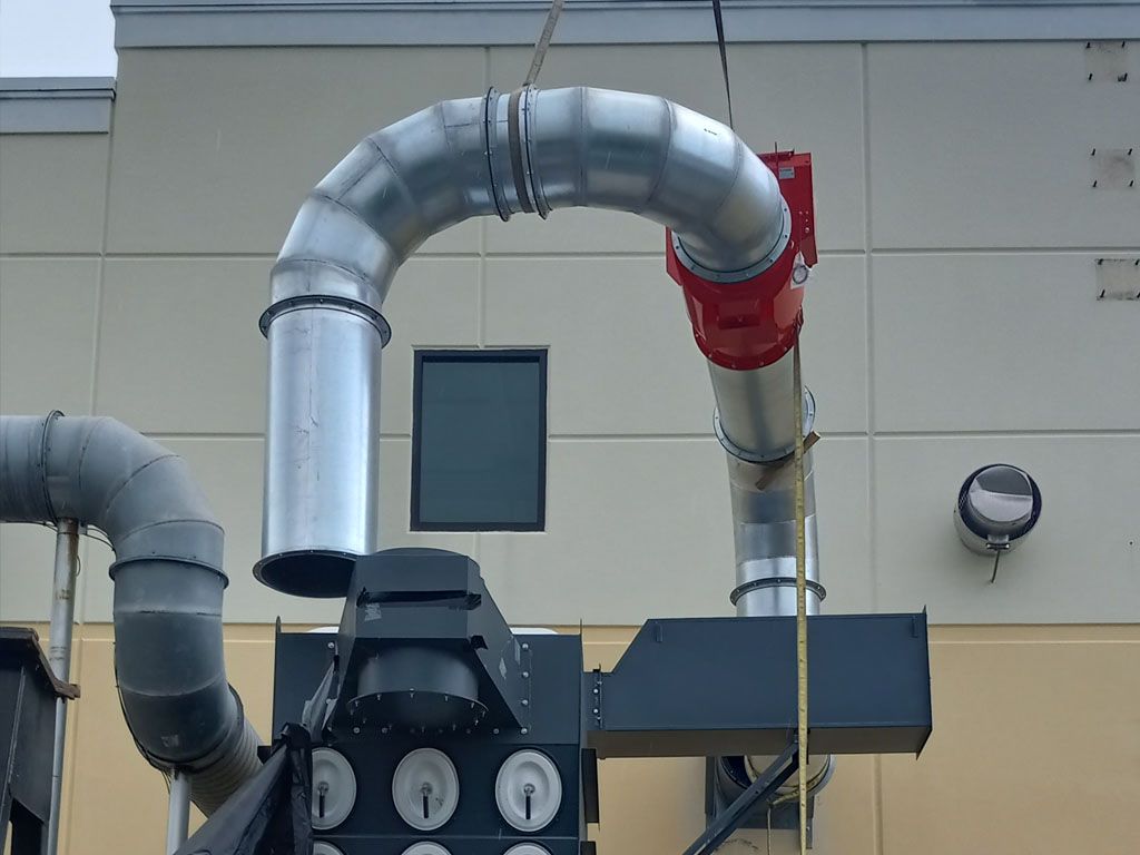 New galvanized industrial ductwork and a red fan housing installed on the outside of a commercial building