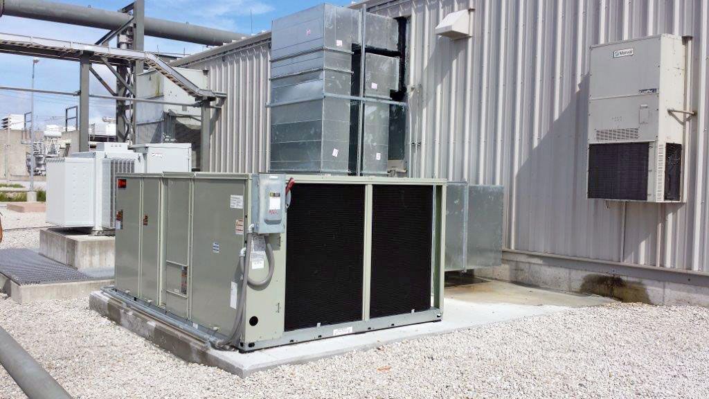 A packaged commercial air conditioning unit installed beside an industrial building and connected to galvanized ductwork