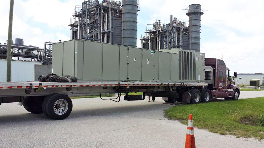 A new commercial air conditioning unit arriving on a flatbed truck at an industrial facility